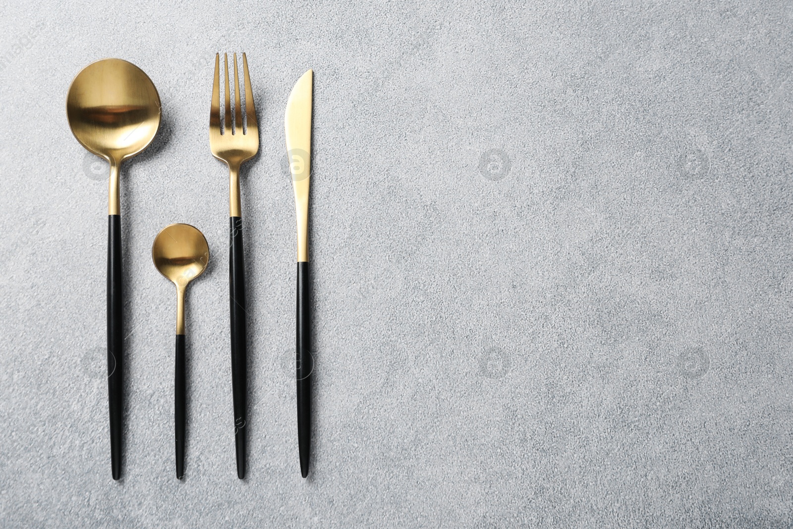 Photo of Stylish golden cutlery on grey table, flat lay. Space for text