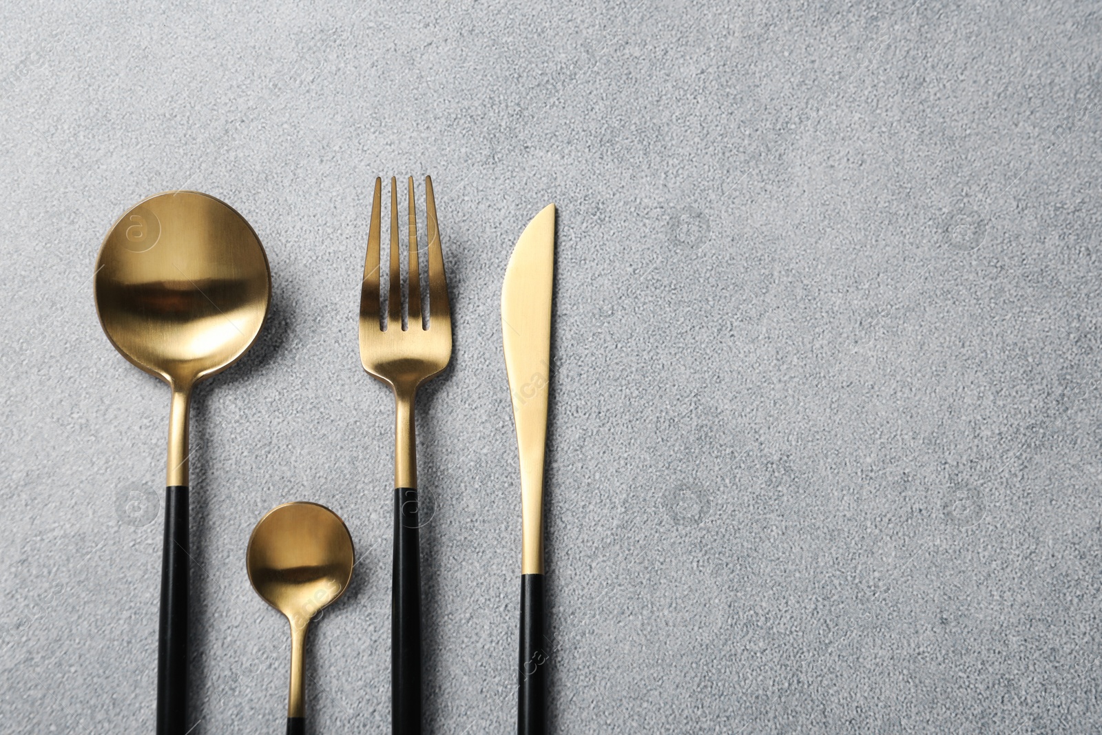 Photo of Stylish golden cutlery on grey table, flat lay. Space for text