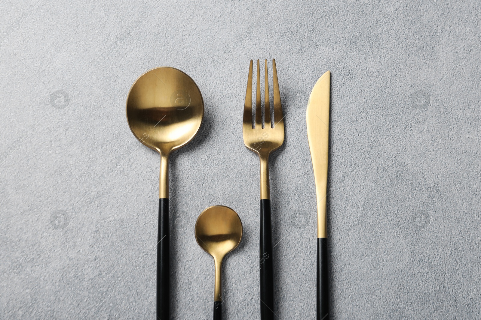 Photo of Stylish golden cutlery on grey table, flat lay