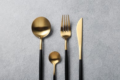 Photo of Stylish golden cutlery on grey table, flat lay