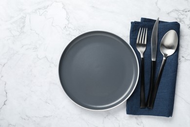 Stylish cutlery, napkin and plate on white marble table, top view. Space for text