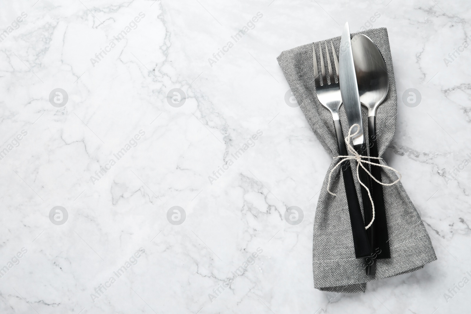 Photo of Stylish cutlery and napkin on white marble table, top view. Space for text