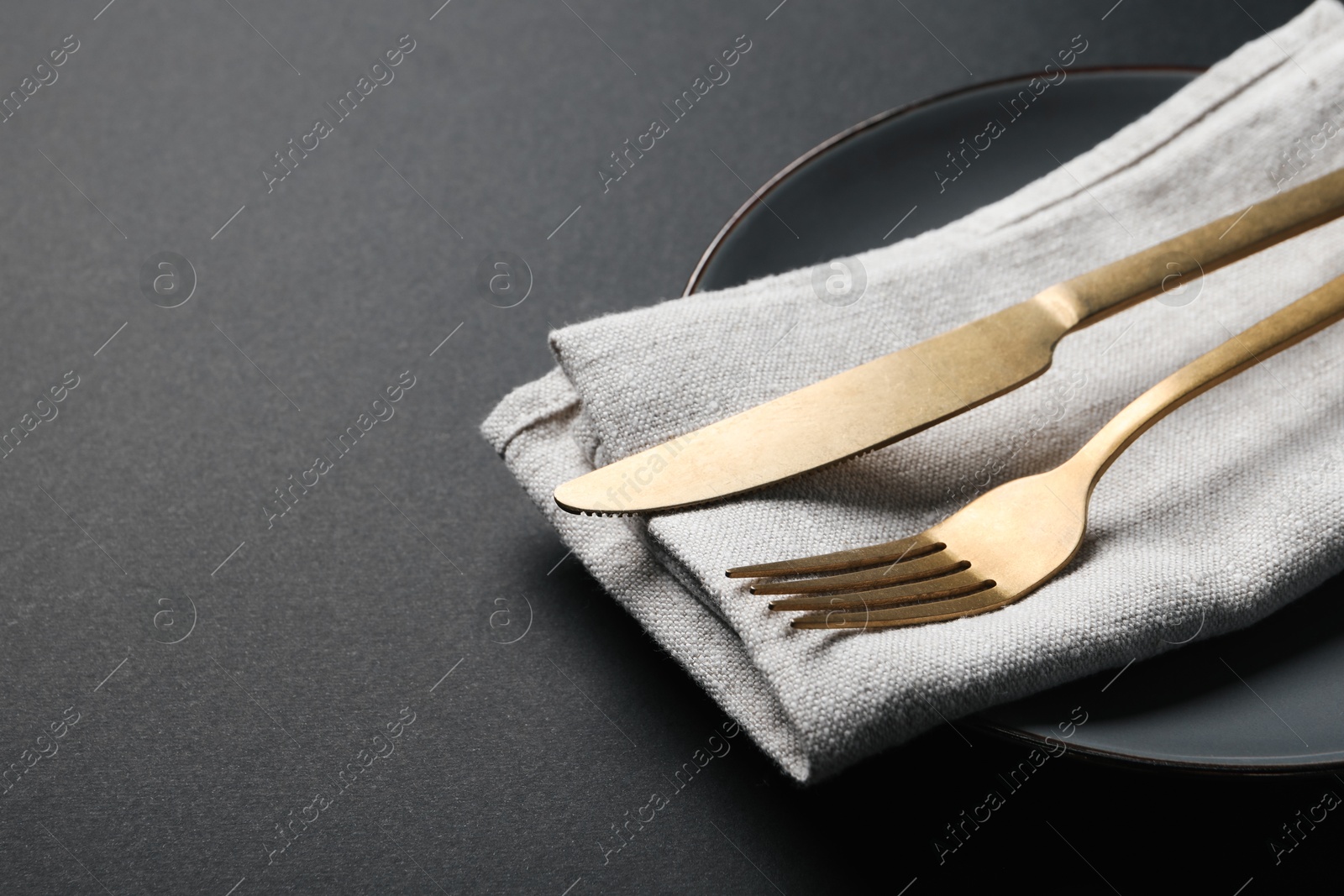 Photo of Elegant golden cutlery, napkin and plate on black background, closeup. Space for text