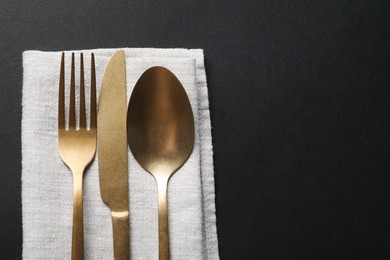 Photo of Elegant golden cutlery and napkin on black background, top view. Space for text