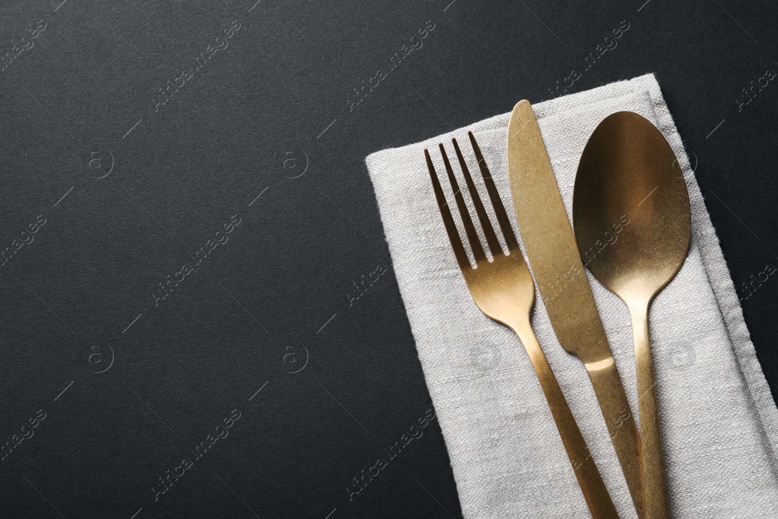 Photo of Elegant golden cutlery and napkin on black background, top view. Space for text