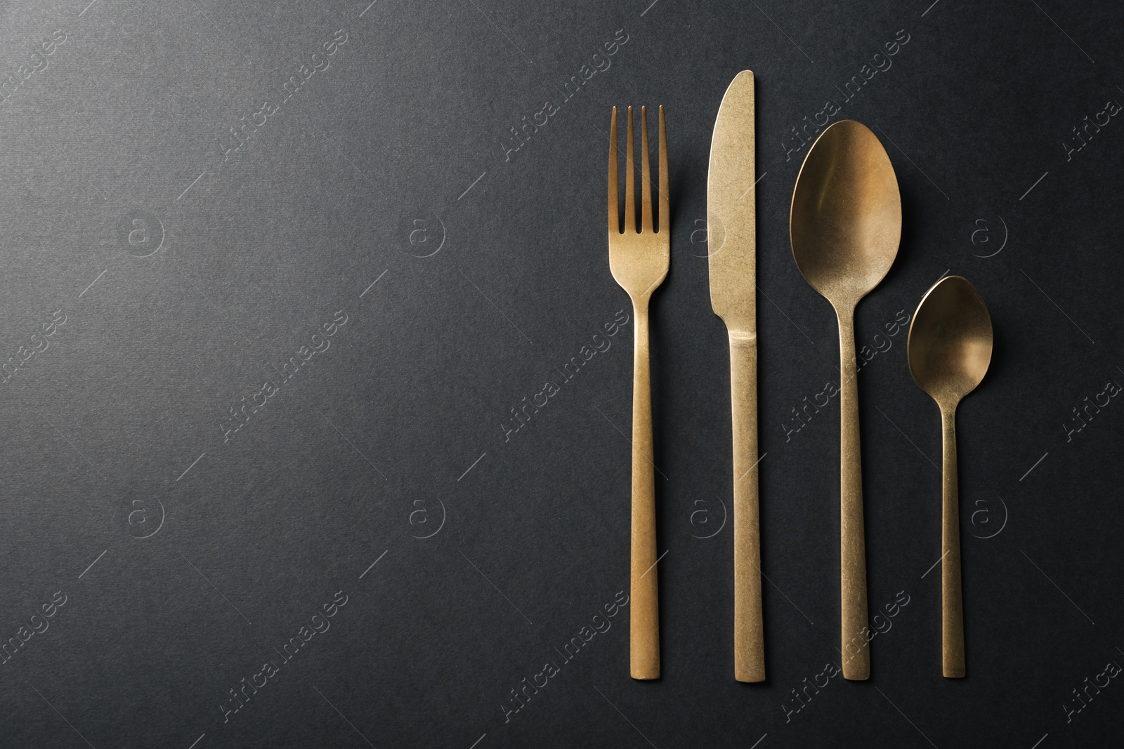 Photo of Elegant golden cutlery on black background, flat lay. Space for text