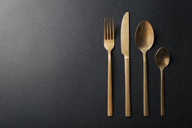 Elegant golden cutlery on black background, flat lay. Space for text