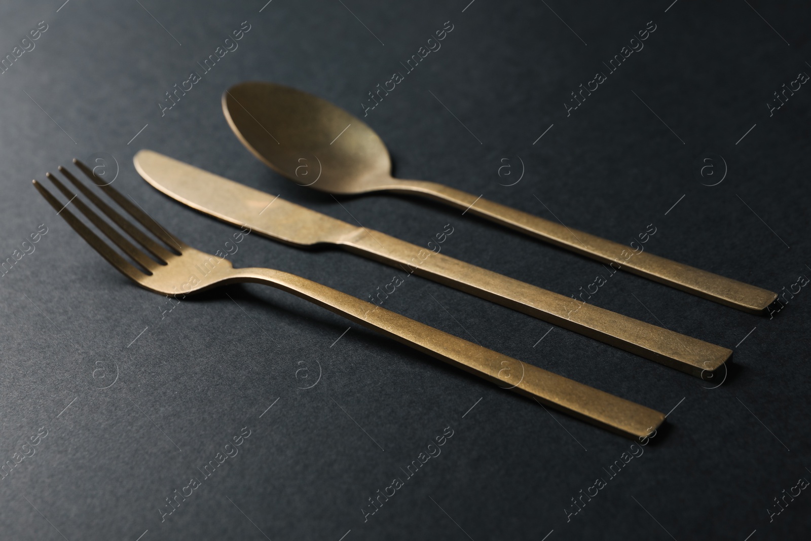 Photo of Elegant golden cutlery. Fork, knife and spoon on black background