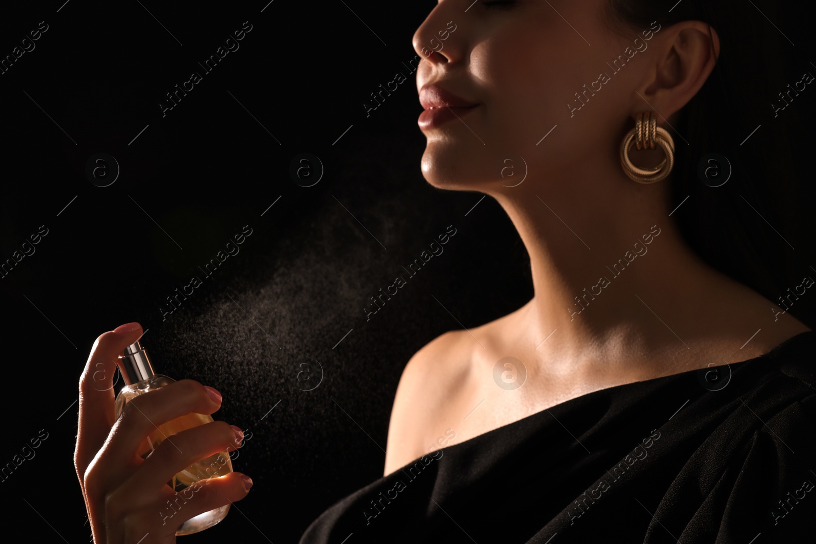 Photo of Woman spraying perfume on black background, closeup