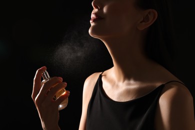 Woman spraying perfume on black background, closeup