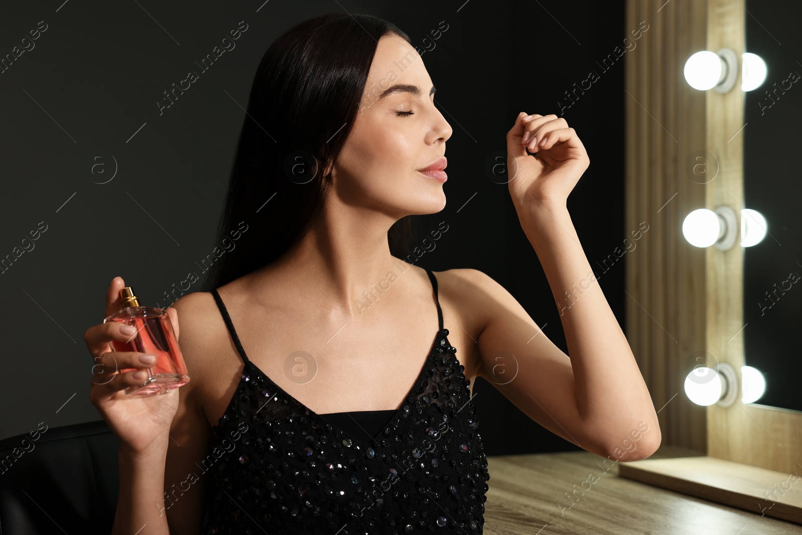 Photo of Beautiful woman smelling perfume on wrist in makeup room