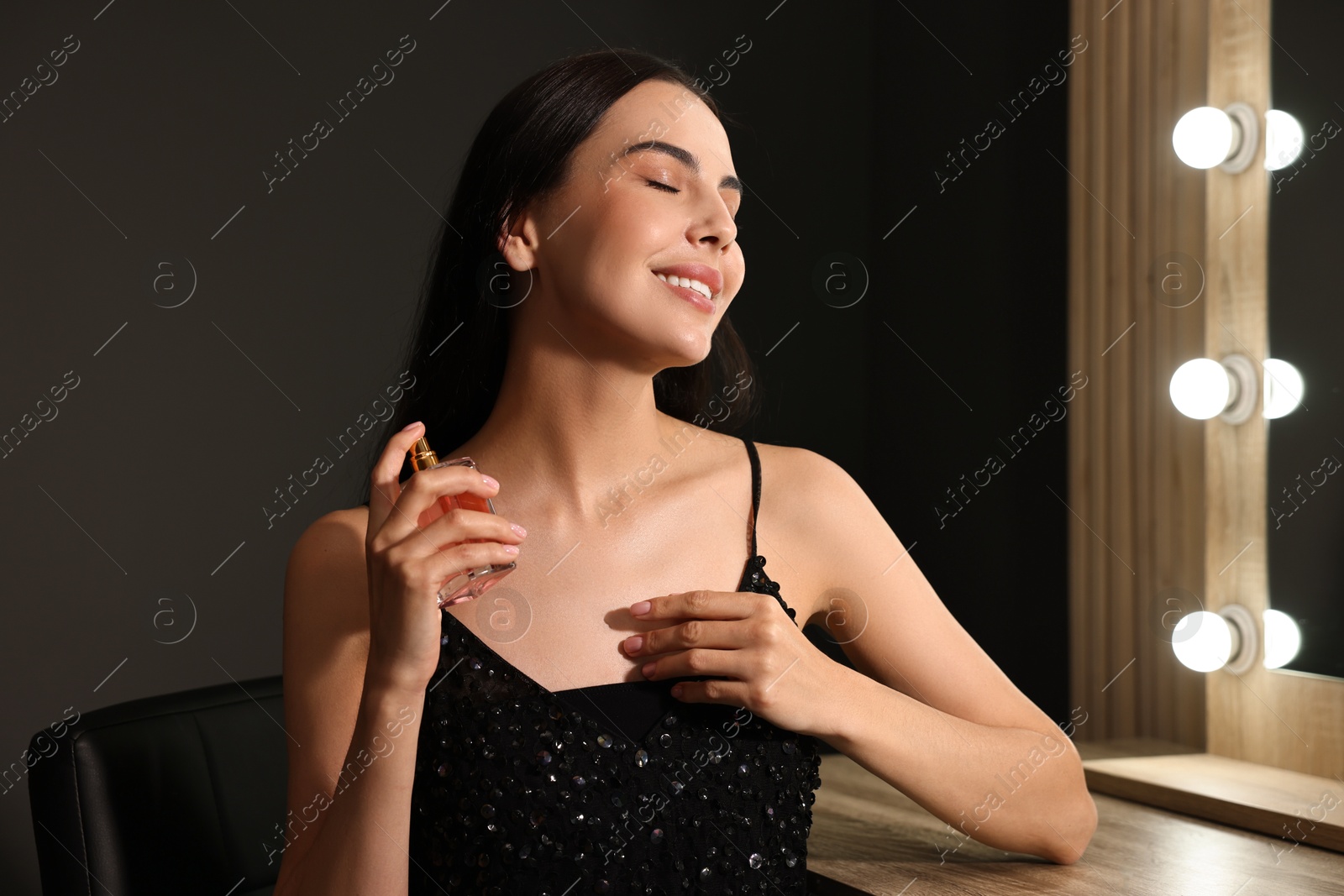 Photo of Smiling woman spraying perfume in makeup room