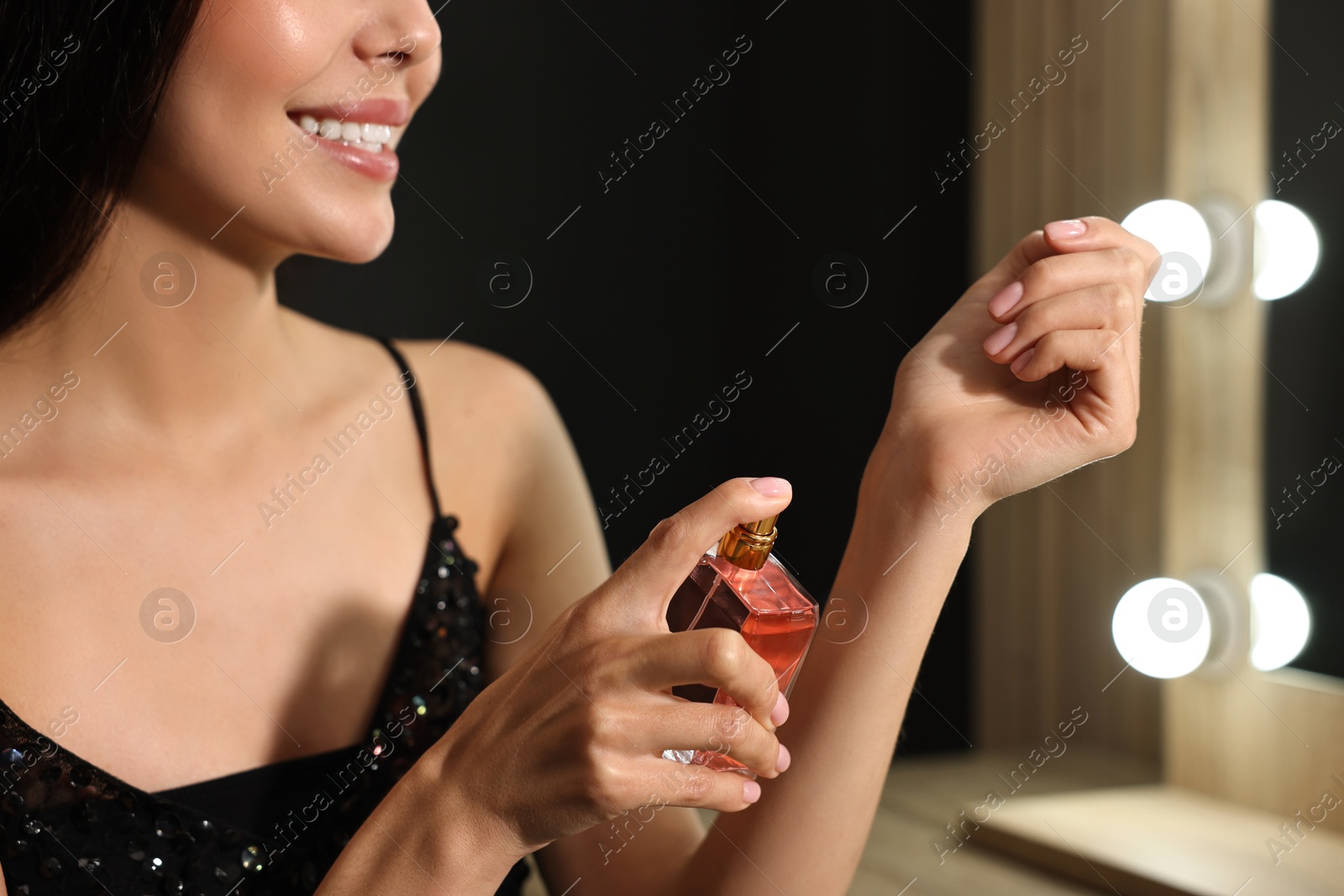 Photo of Smiling woman spraying perfume at home, closeup