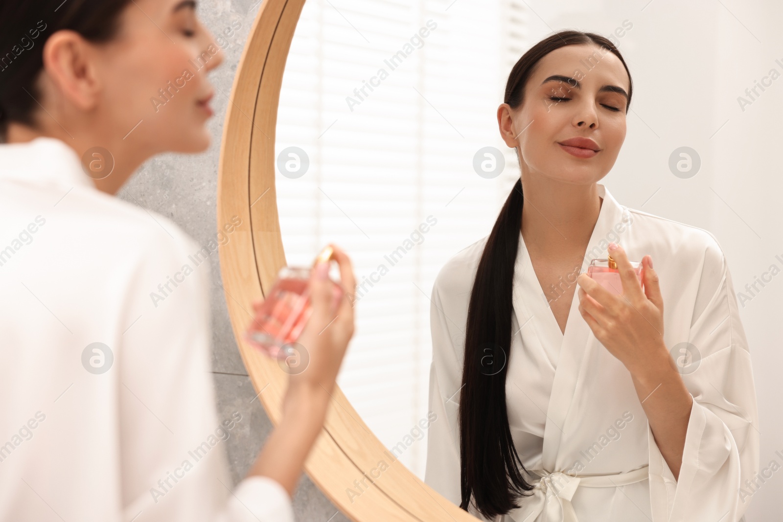 Photo of Beautiful woman spraying perfume near mirror in bathroom