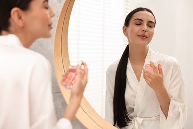 Beautiful woman spraying perfume near mirror in bathroom