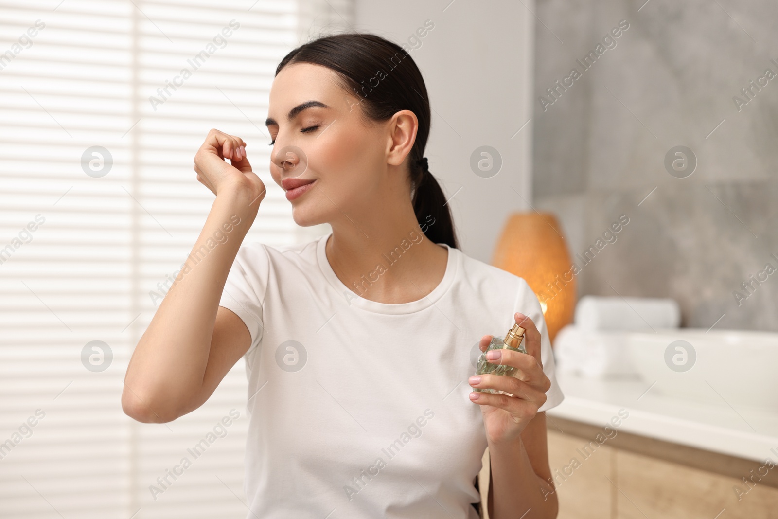 Photo of Beautiful woman smelling aromatic perfume in bathroom