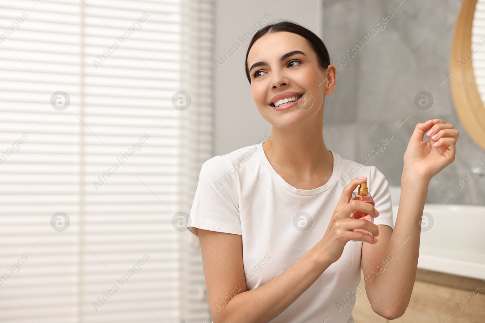 Photo of Smiling woman spraying perfume indoors. Space for text