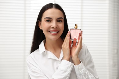 Smiling woman with bottle of perfume at home