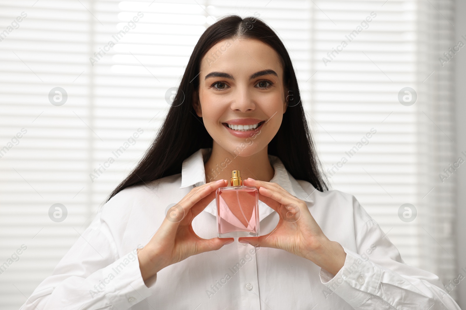 Photo of Smiling woman with bottle of perfume at home