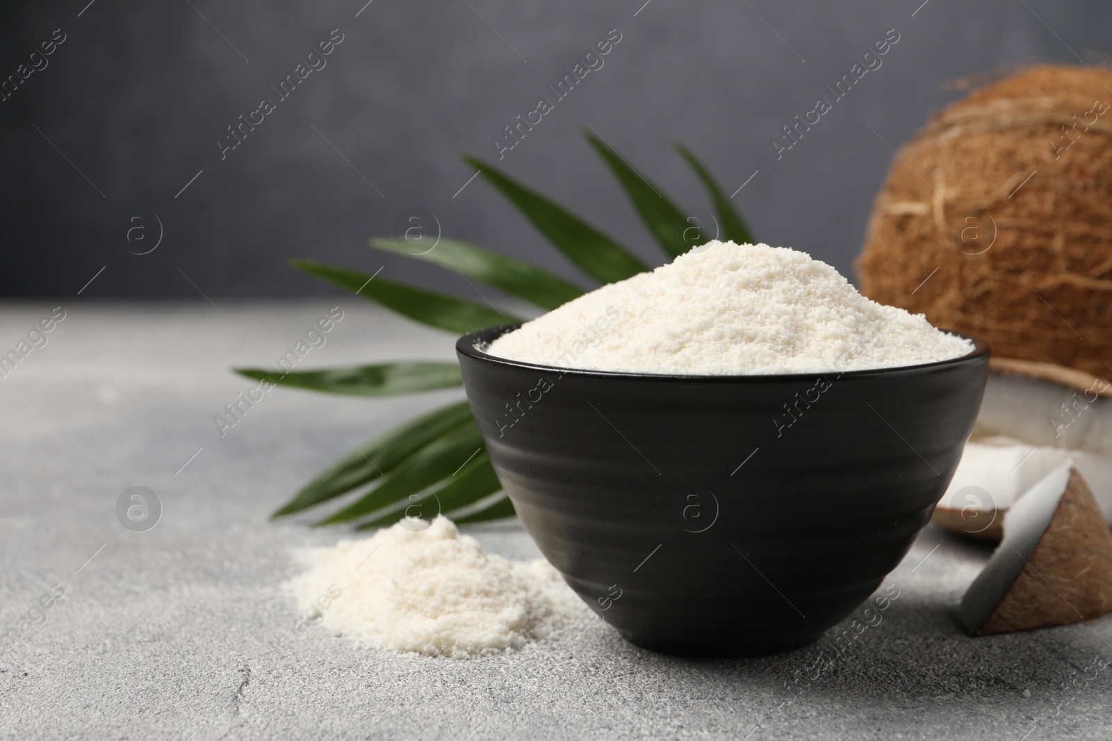 Photo of Coconut flour in bowl on light grey table, closeup. Space for text