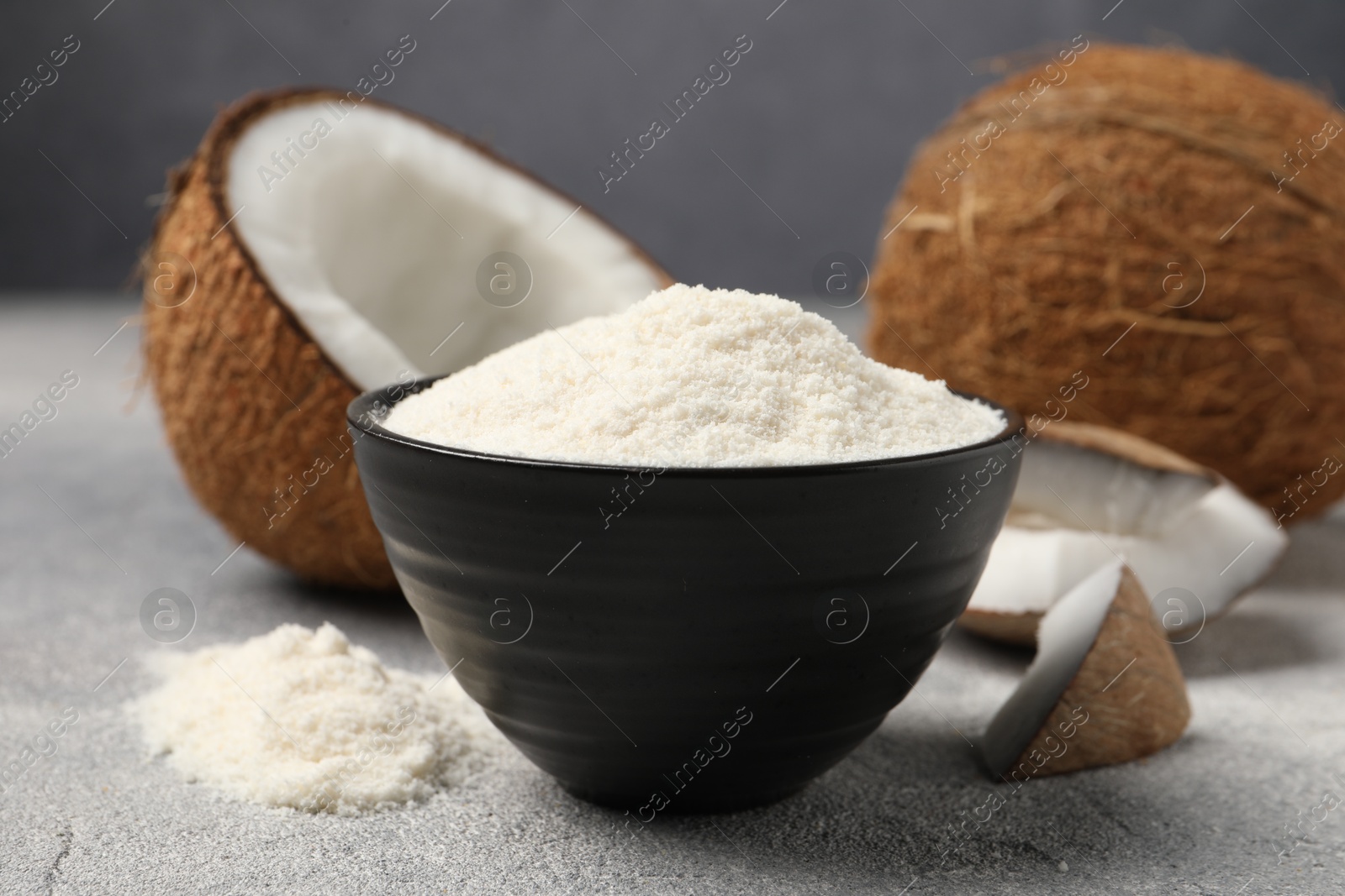 Photo of Coconut flour in bowl and fresh fruits on light grey table, closeup