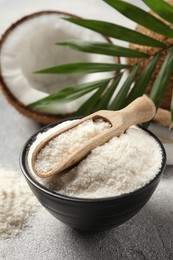 Photo of Coconut flour in bowl, scoop, fresh fruits and leaf on light grey table