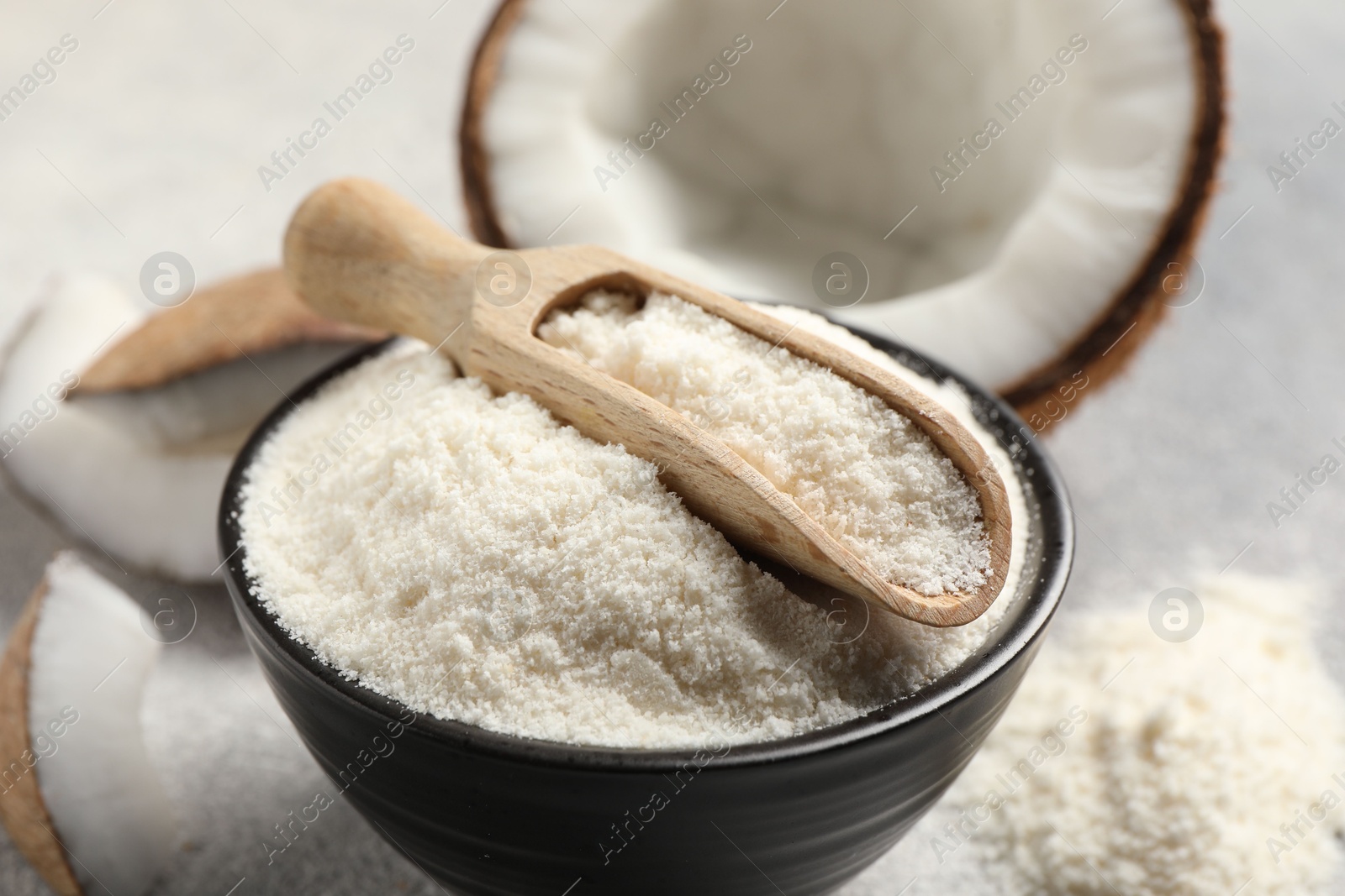 Photo of Coconut flour in bowl and scoop on light grey table, closeup