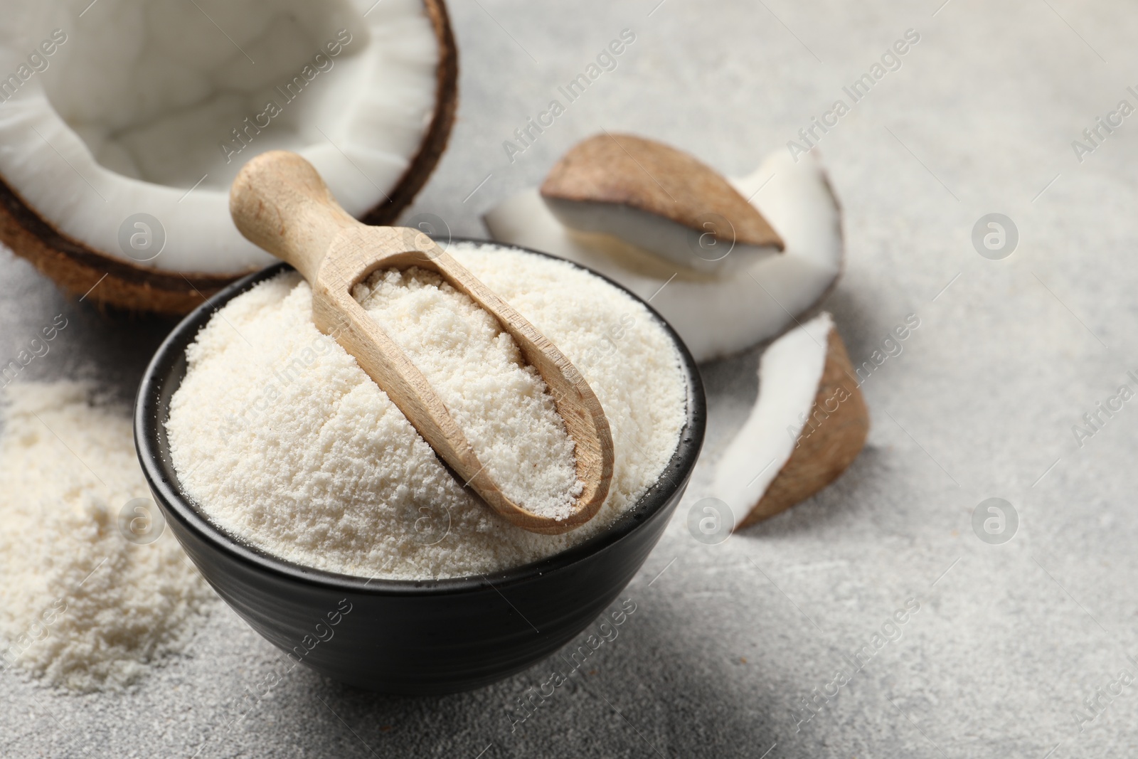 Photo of Coconut flour in bowl, scoop and fresh fruits on light grey table, closeup