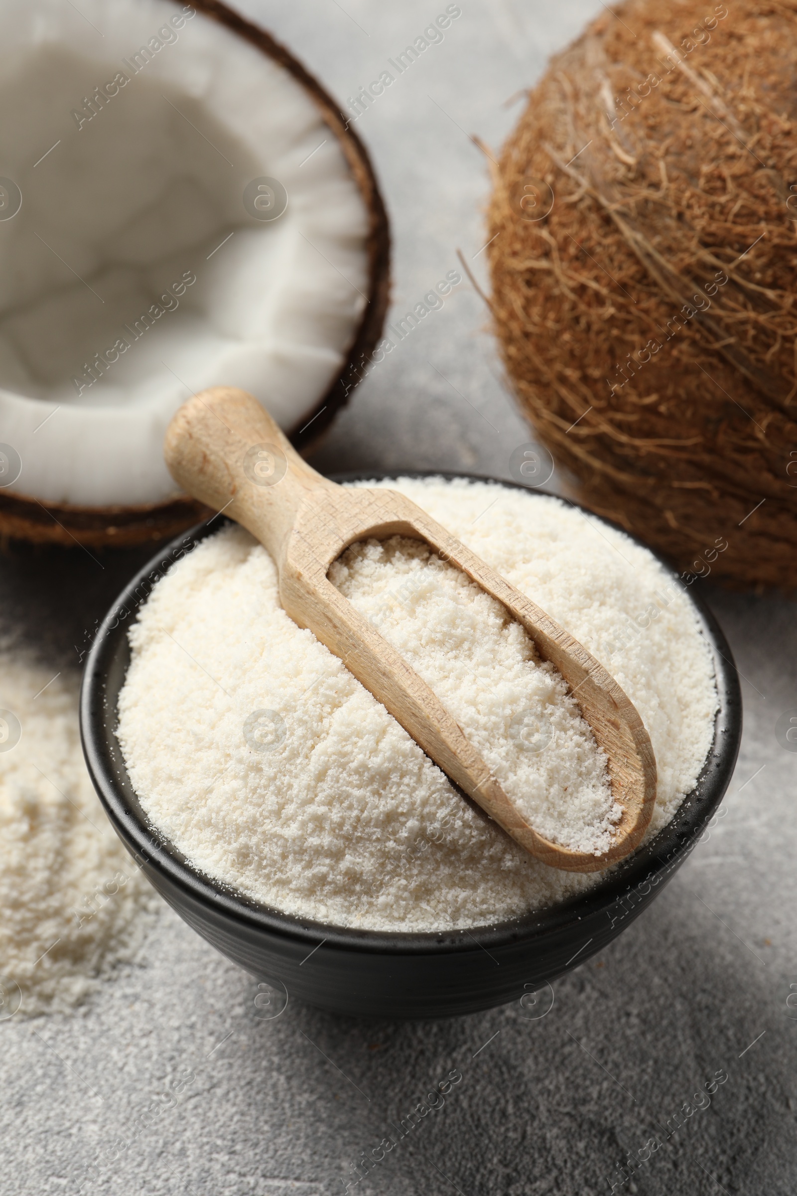 Photo of Coconut flour in bowl, scoop and fresh fruits on light grey table, closeup