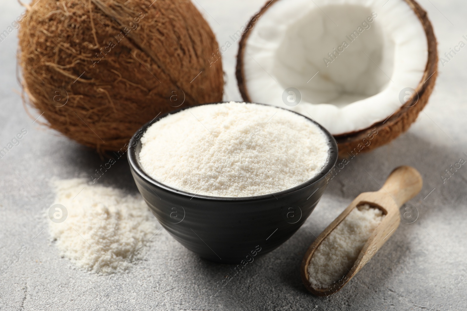 Photo of Coconut flour in bowl, scoop and fresh fruits on light grey table, closeup