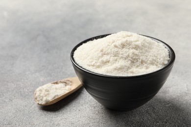 Photo of Coconut flour in bowl and spoon on light grey table, closeup