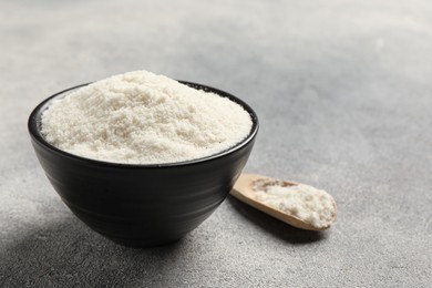 Photo of Coconut flour in bowl and spoon on light grey table, closeup. Space for text