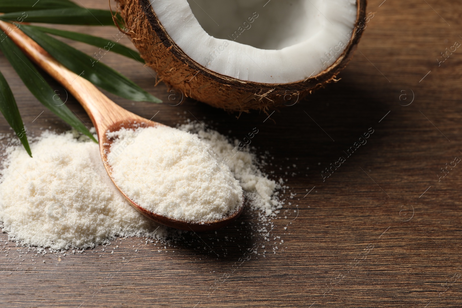 Photo of Coconut flour in spoon and fresh fruit on wooden table, closeup. Space for text