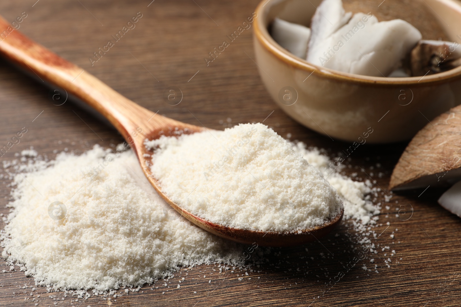 Photo of Coconut flour in spoon and fruit pieces on wooden table, closeup