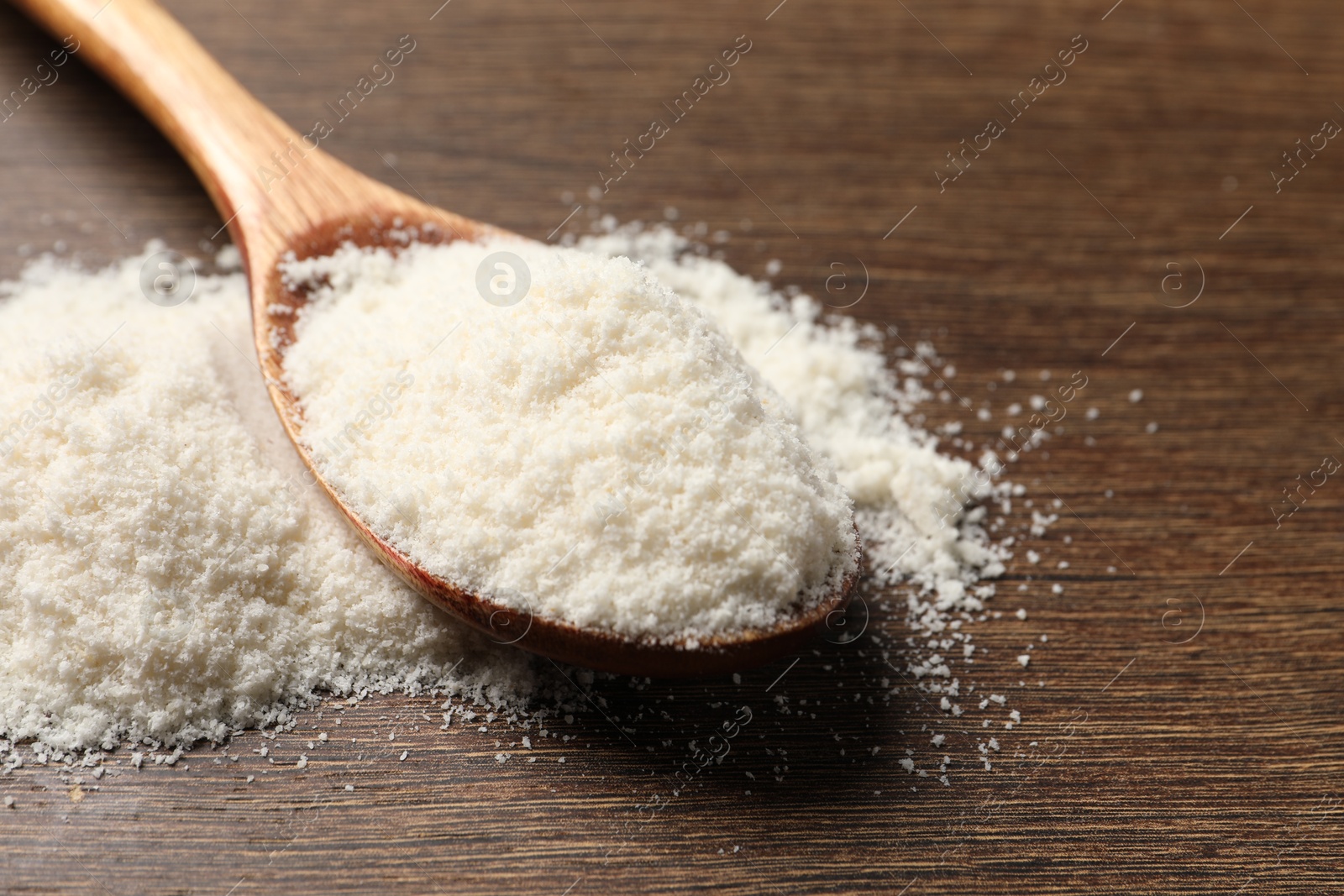 Photo of Coconut flour in spoon on wooden table, closeup