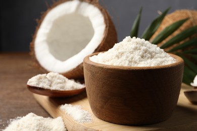 Photo of Coconut flour in bowl, spoon and fresh fruits on wooden table, closeup