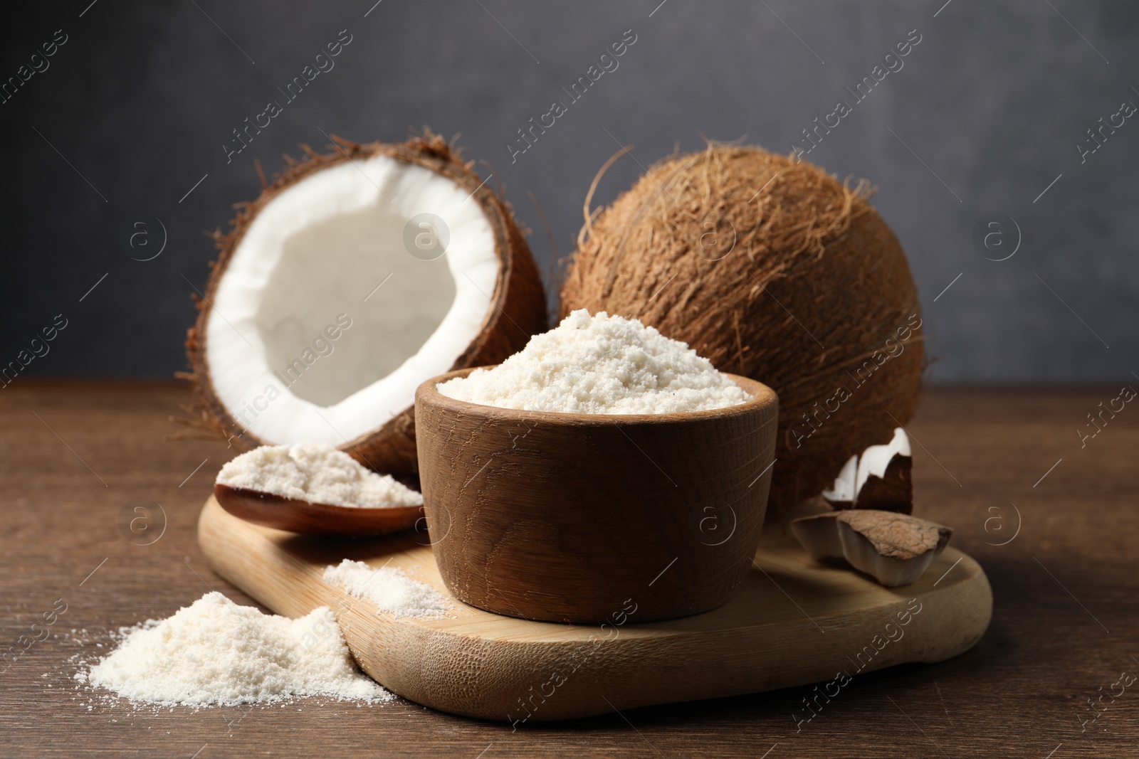 Photo of Organic coconut flour in bowl, spoon and fresh fruits on wooden table