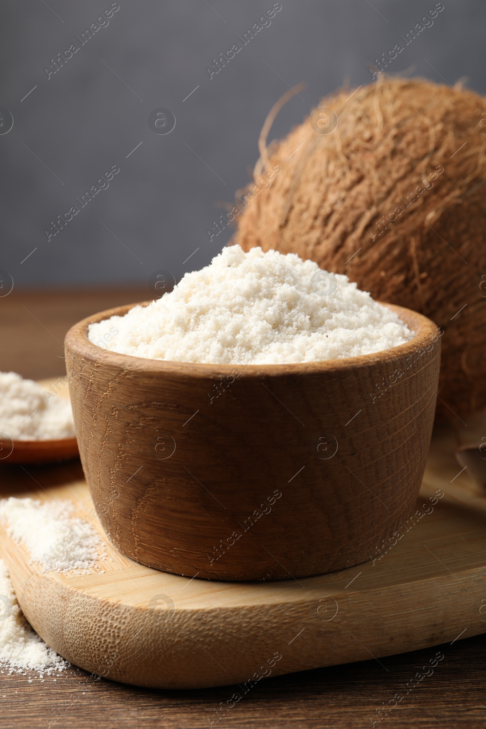 Photo of Organic coconut flour in bowl and fresh fruit on wooden table, closeup