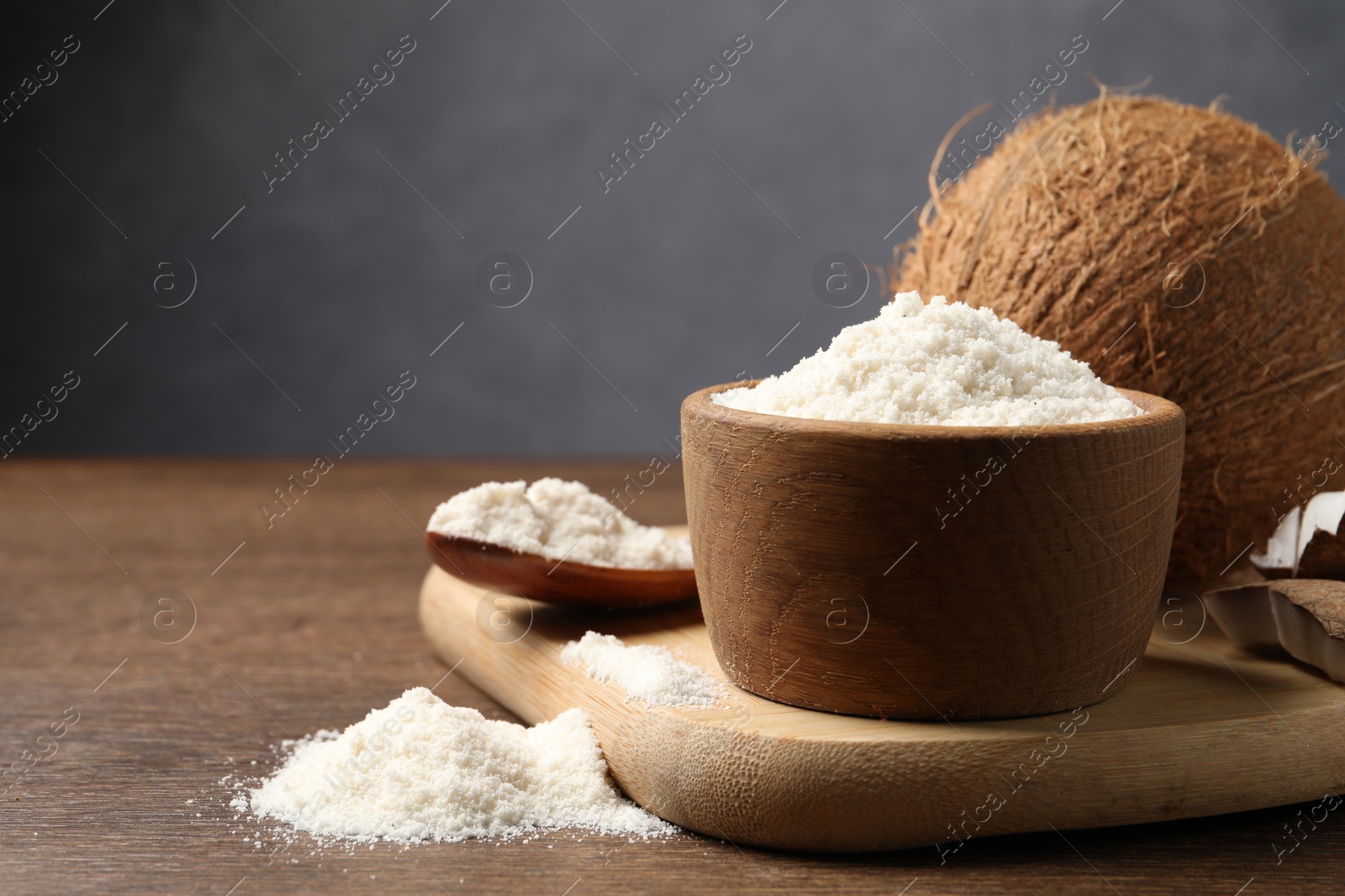 Photo of Organic coconut flour in bowl, spoon and fresh fruit on wooden table, closeup. Space for text