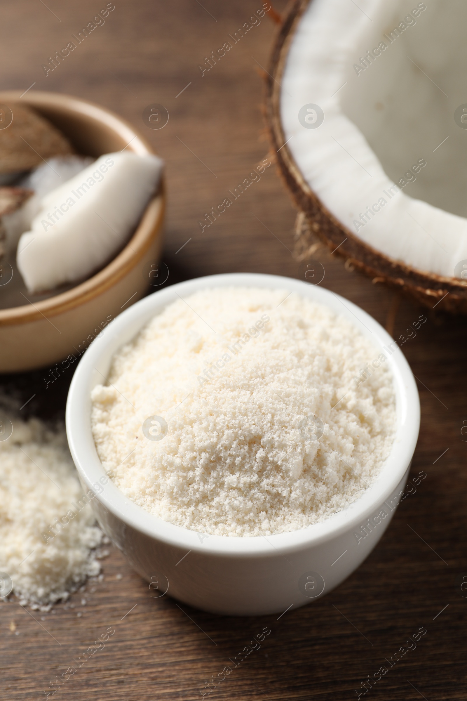 Photo of Coconut flour in bowl and fresh fruit on wooden table, closeup