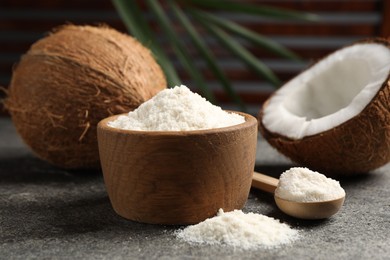 Photo of Organic coconut flour in bowl, spoon and fresh fruits on grey table, closeup