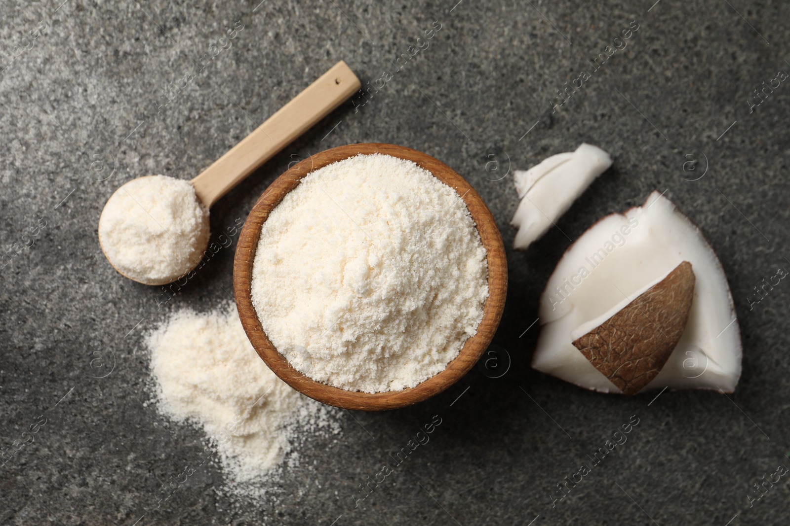 Photo of Organic coconut flour in bowl, spoon and fruit pieces on grey table, flat lay