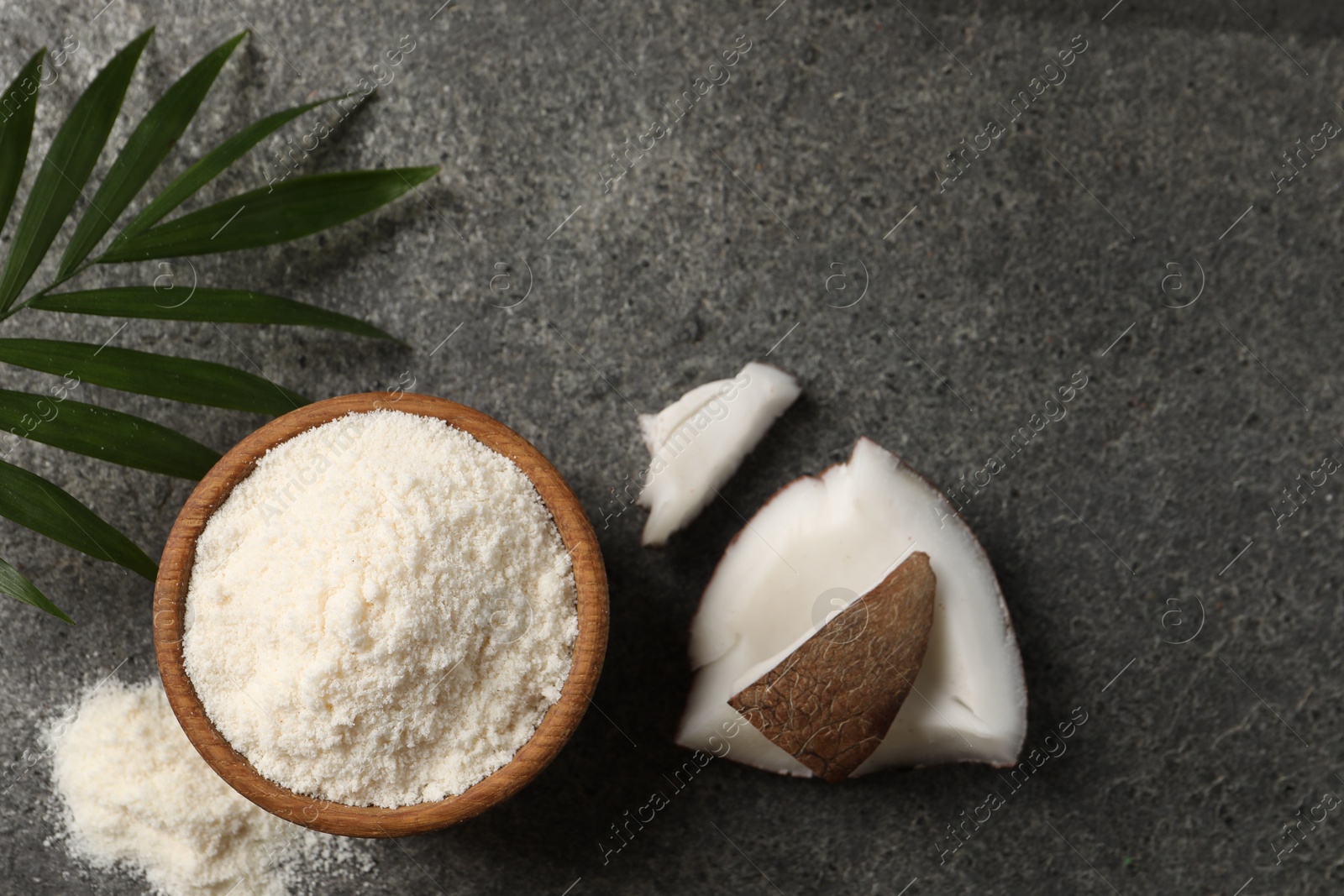 Photo of Organic coconut flour in bowl, fruit pieces and leaf on grey table, flat lay. Space for text