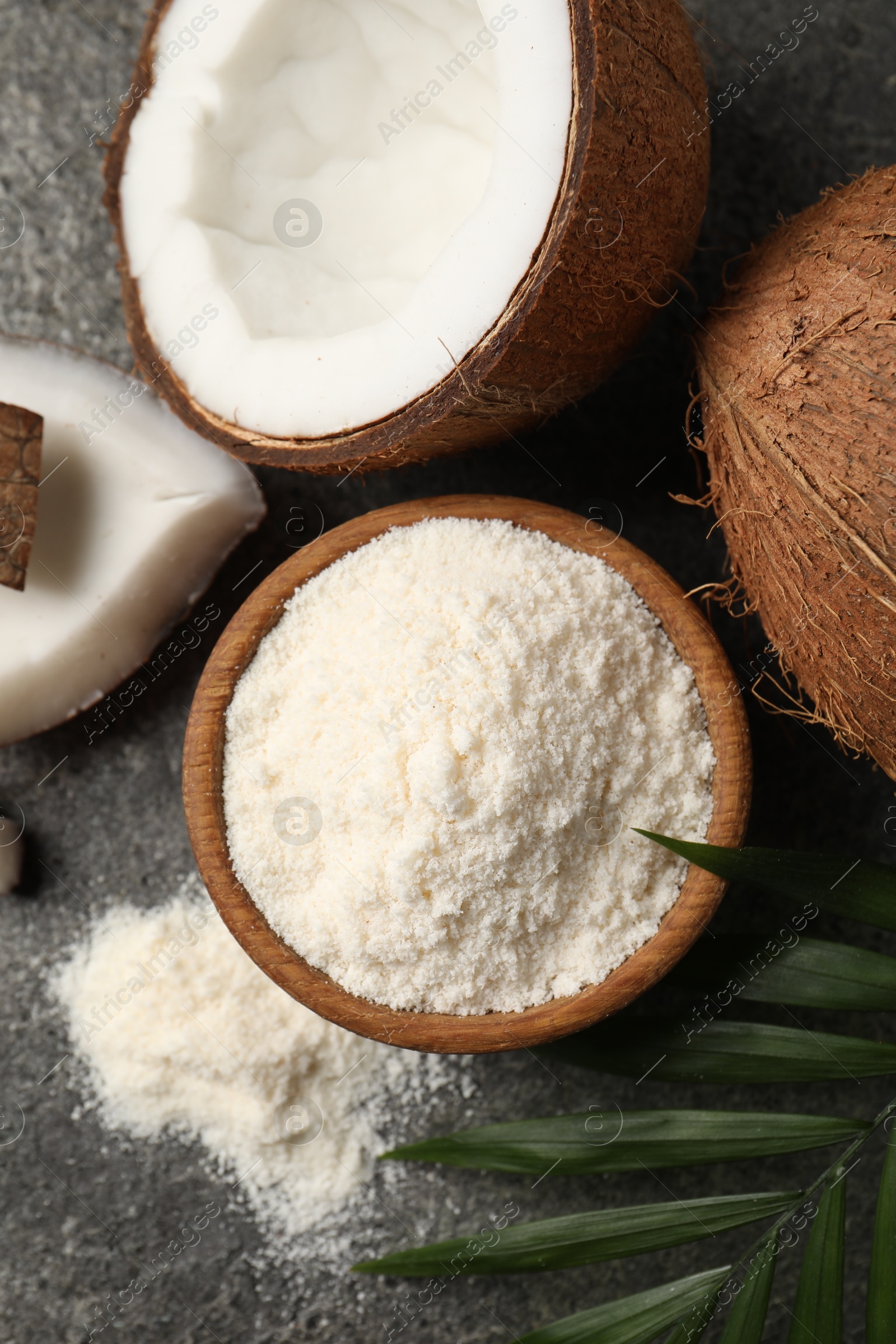 Photo of Organic coconut flour in bowl, fresh fruits and leaf on grey table, flat lay