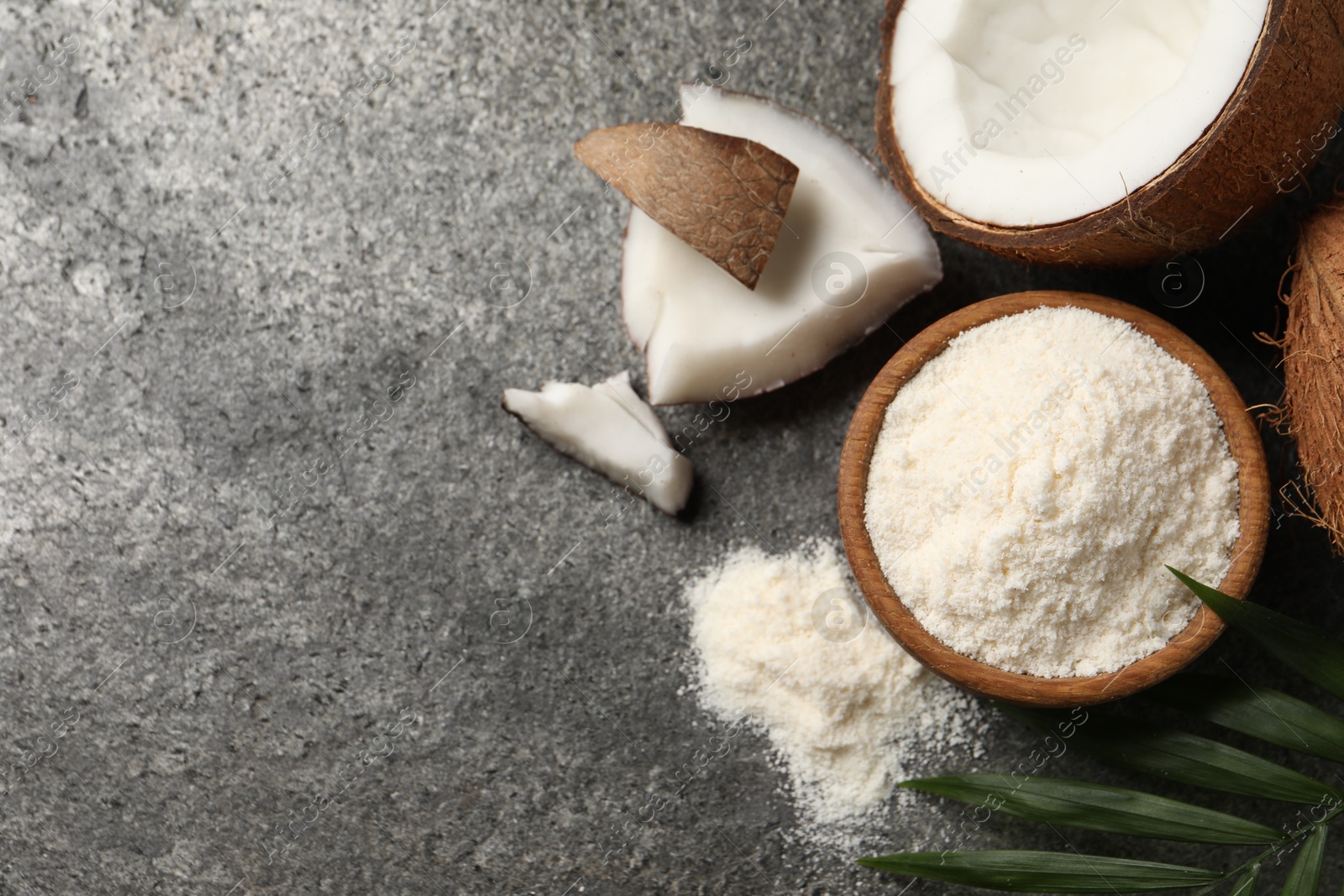 Photo of Organic coconut flour in bowl, fresh fruits and leaf on grey table, flat lay. Space for text