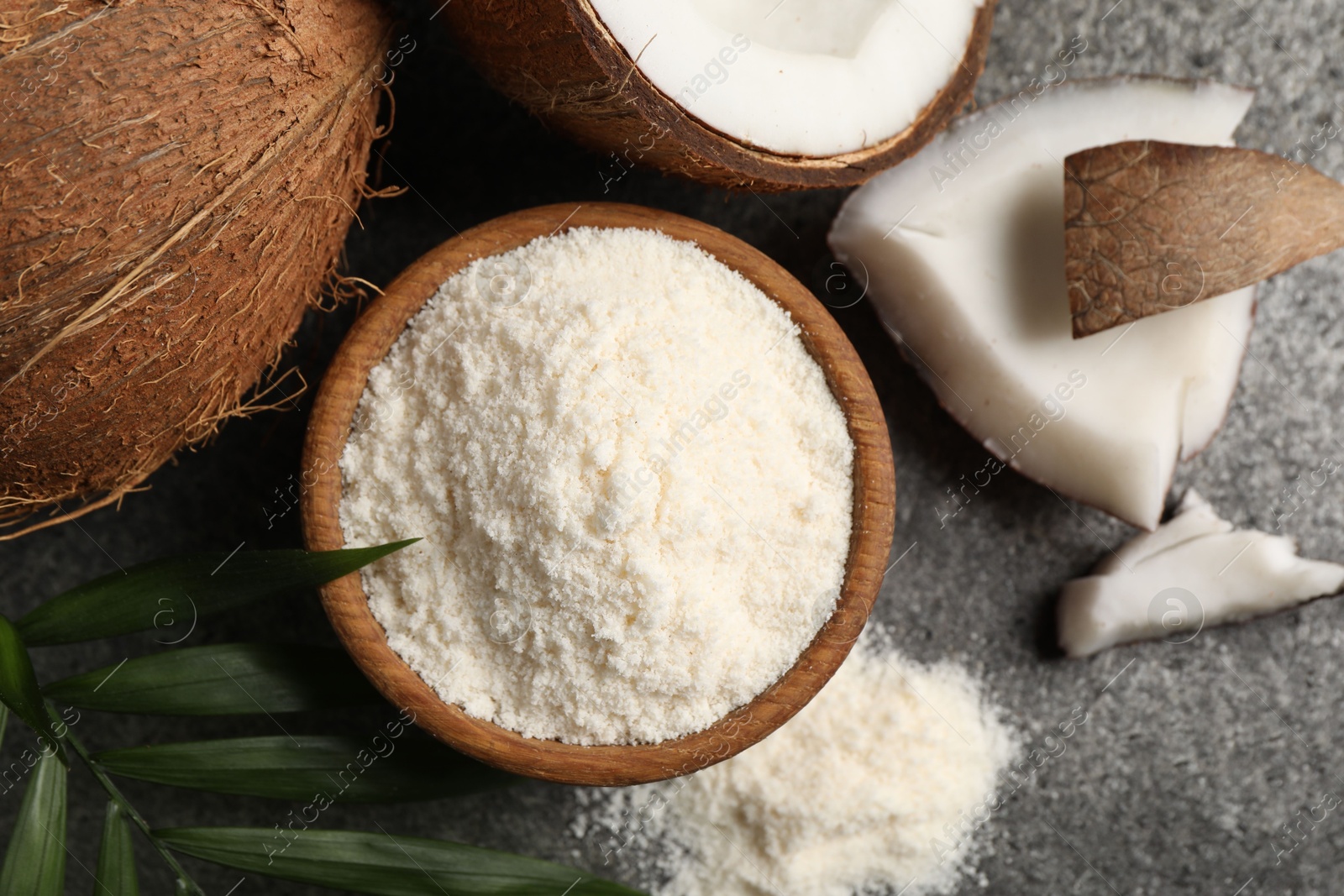 Photo of Organic coconut flour in bowl, fresh fruits and leaf on grey table, flat lay