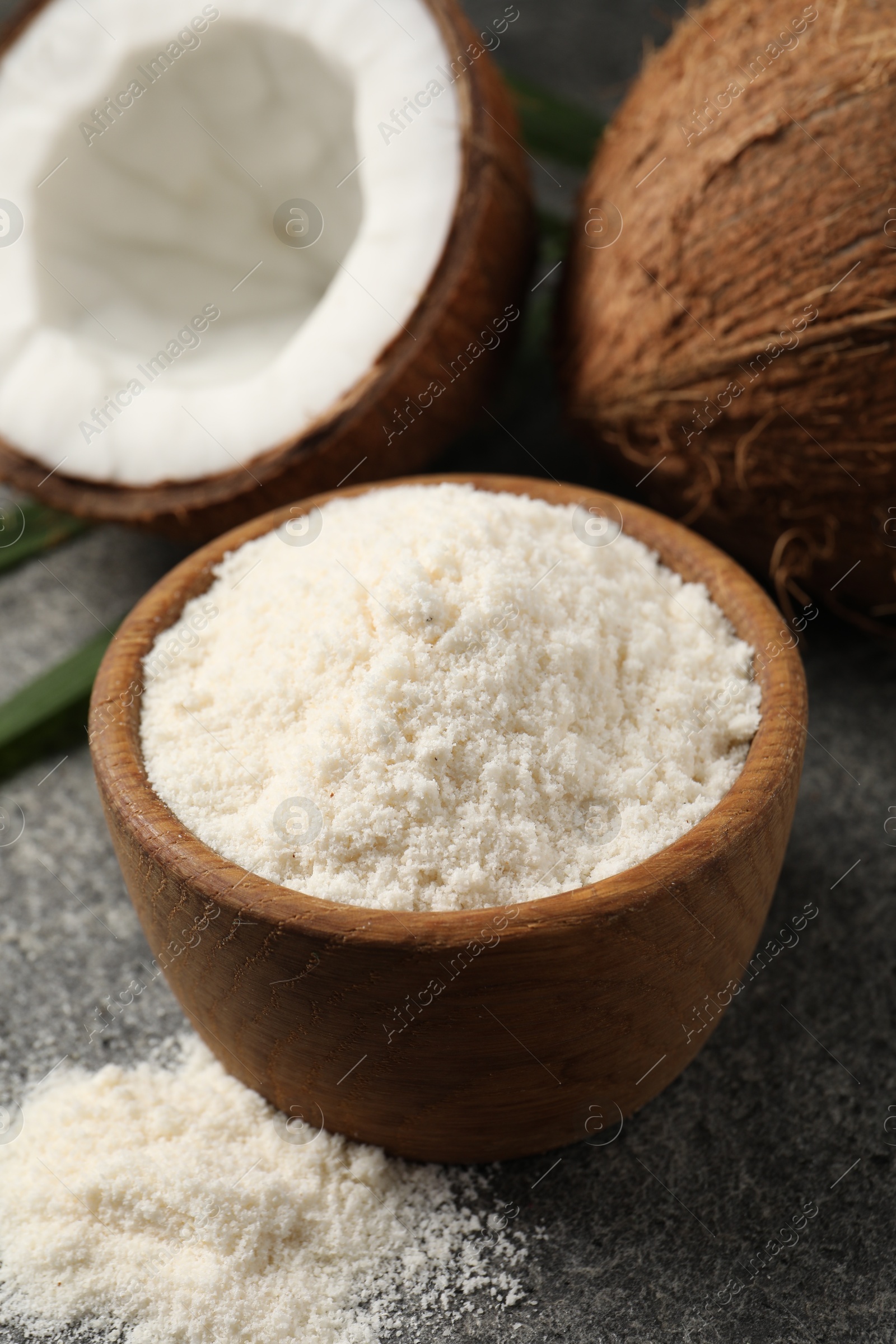 Photo of Organic coconut flour in bowl and fresh fruits on grey table, closeup