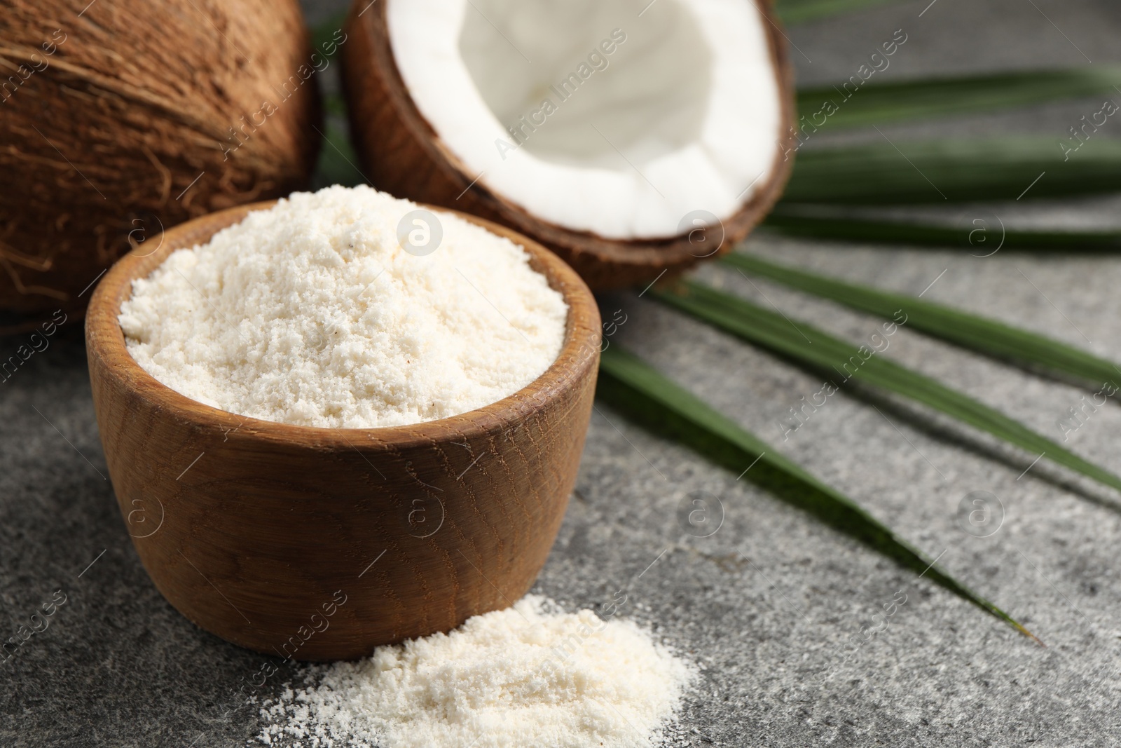 Photo of Organic coconut flour in bowl, fresh fruits and leaf on grey table, closeup