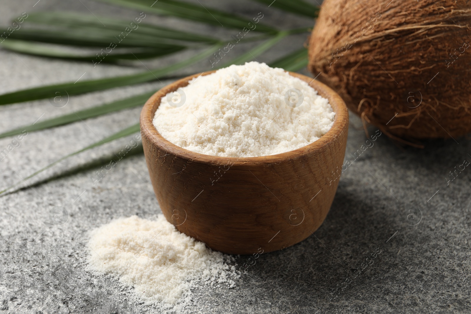 Photo of Organic coconut flour in bowl, fresh fruit and leaf on grey table, closeup