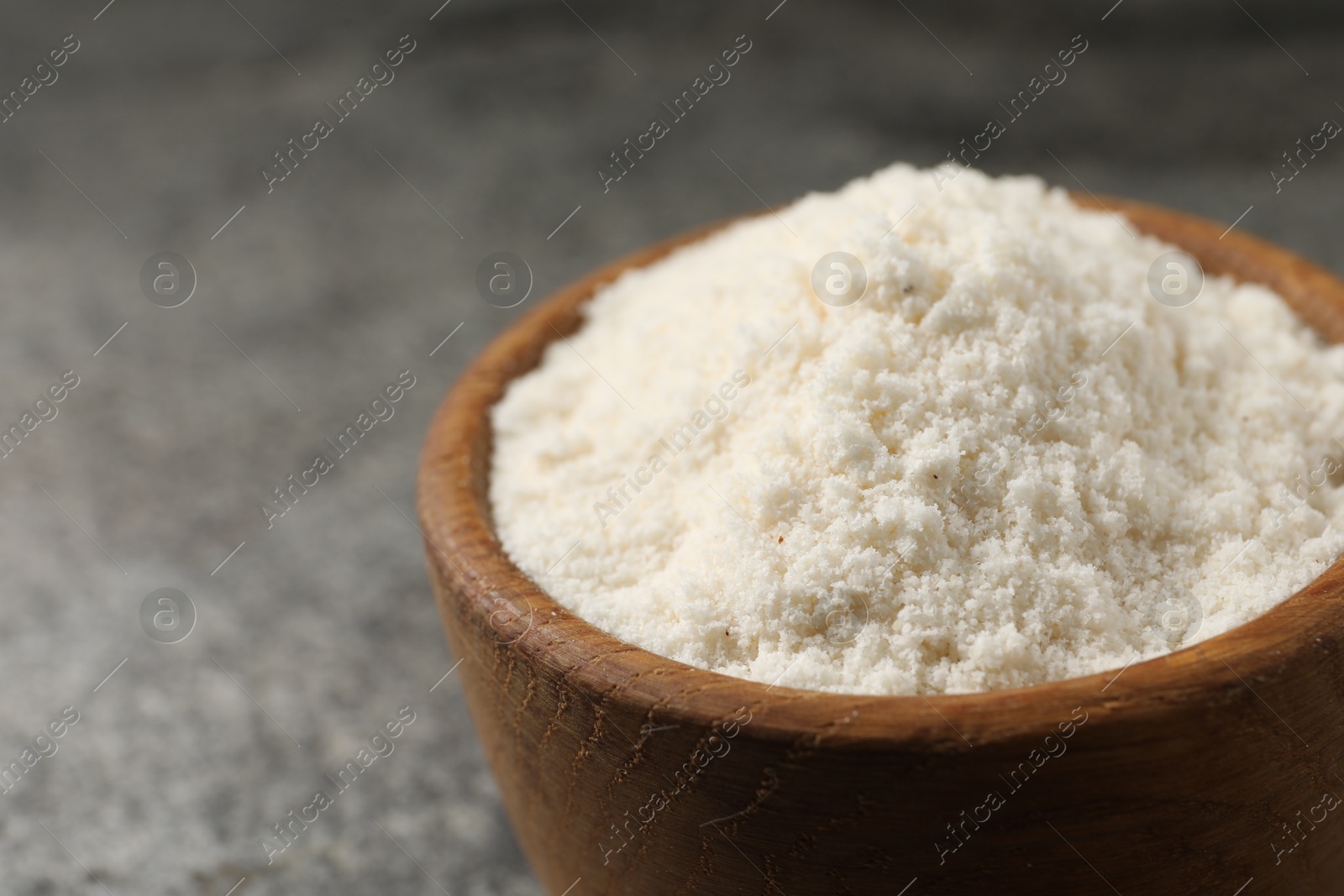 Photo of Organic coconut flour in bowl on grey table, closeup. Space for text